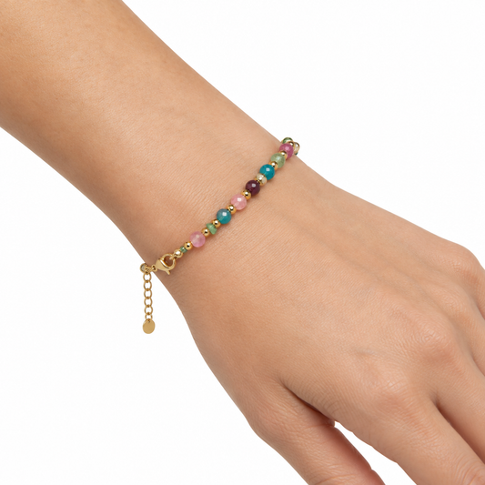 Delikatna bransoletka z fasetowanych kolorowych kamieni na nadgarstku, biale tlo